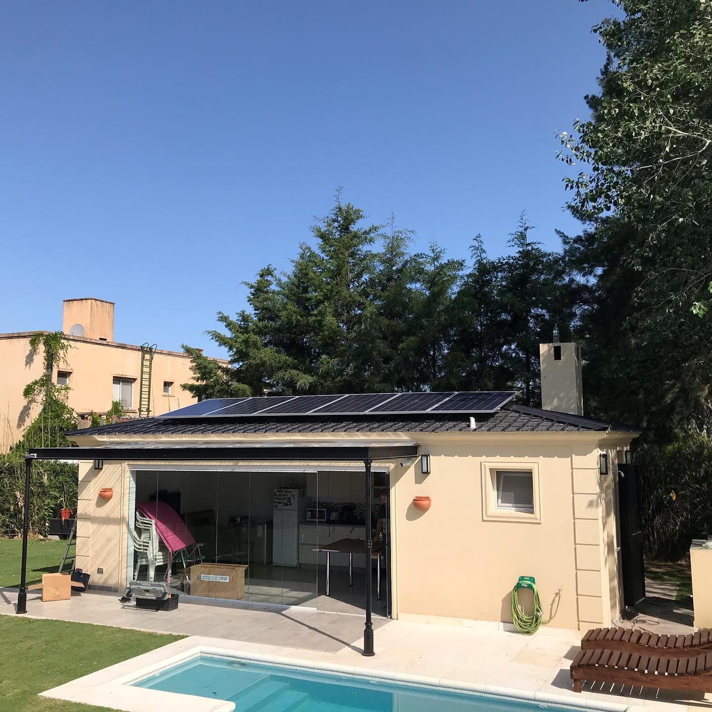 Casa con pileta y una fila de paneles sobre el techo de tejas negras.